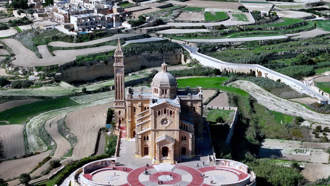 Majestic aerial view of Ta' Pinu National Shrine in Gozo Malta standing as a Romanesque masterpiece amidst lush green spring fields under bright sunlight capturing the spiritual heritage of Gharb