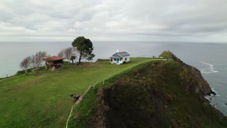 Small-blue-and-white-church-next-in-a-cliff-to-the-sea,-Ermita-de-la-Regalina,-above-the-steep-cliffs-on-the-coast-of-Asturias,-North-Spain