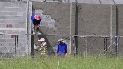 two workers applying cement on a wall.