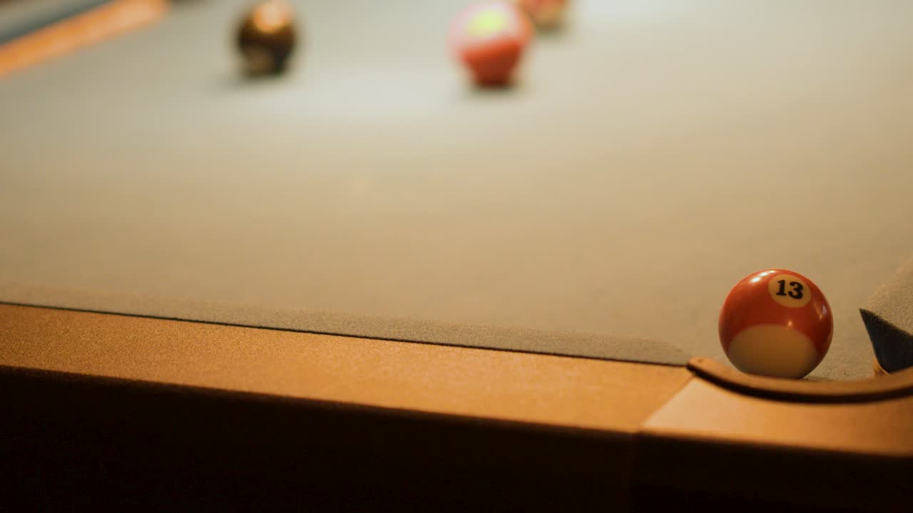 Number 13 billiard ball rolls and drops into corner pocket under warm, low lighting