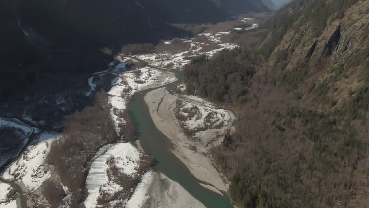 Drone footage pan up of green river to snow capped mountains in a large valley 4k Footage