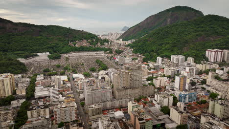 botafogo, rio de janeiro, contrast between dense cityscape and sprawling são joão batista cemetery at the base of lush green mountains, brazil. aerial forward