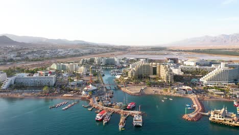 multiple big hotels and resorts at the boulevard of eilat with a mountain view and sea view on a bright sunny day. drone panning shot