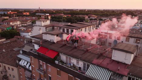 Drone-shot-of-a-group-of-people-dressed-in-black-with-some-red-smoke-bombs-on-a-rooftop-at-sunrise