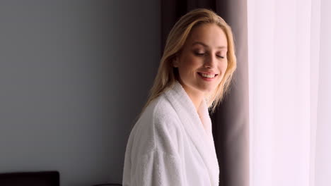 blonde woman smiling near window in hotel room.