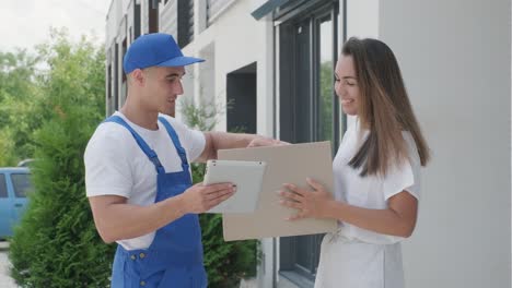 una mujer hermosa conoce a un repartidor que le da una caja de paquetes al lado de su casa, el mensajero comprueba la información en la tableta. entrega a domicilio, compras en línea