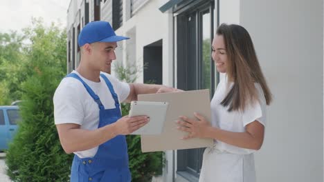 beautiful woman meets a delivery man who gives her a parcel box beside her home, courier checks information on tablet. home delivery, online shopping