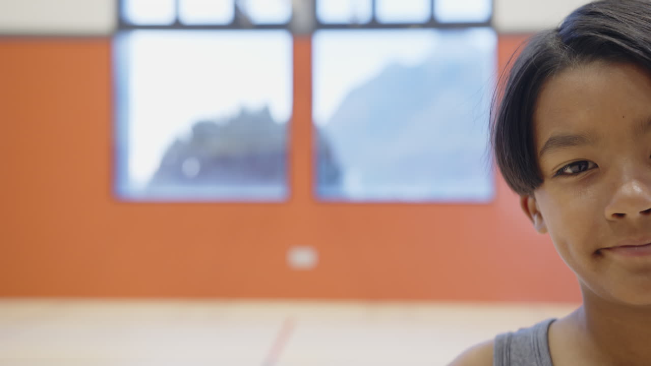 In school gym, boy standing and looking at camera, focusing on activity