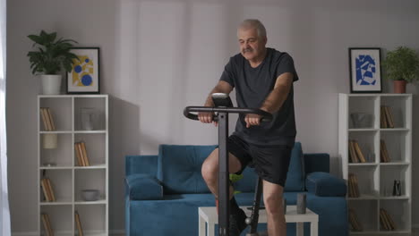 home fitness and healthy lifestyle of middle-aged man is training on stationary bike in apartment cardio workout for keeping good physical condition