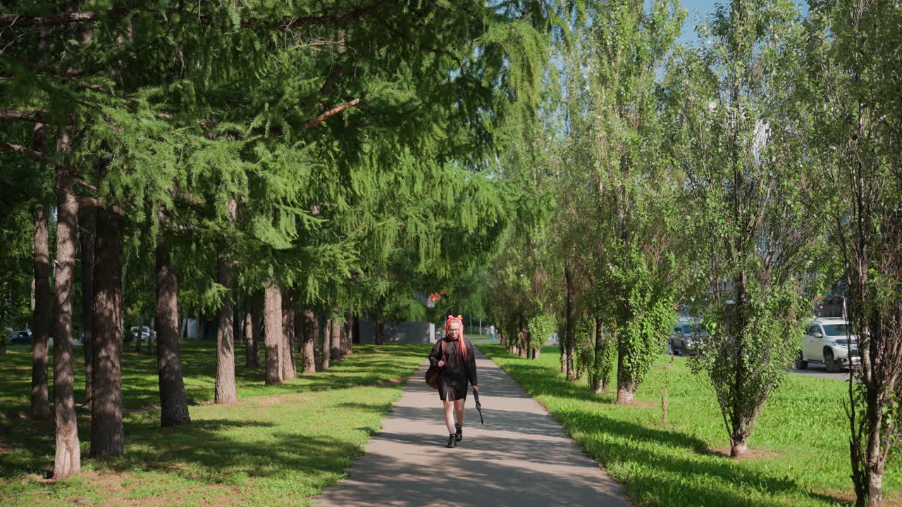 mensajero a pie, hombre entregando un paquete por un sendero en un parque, mensajero blanco moviéndose por un parque de la ciudad con un paquete en la mano, persona caucásica transportando un paquete por un corredor urbano verde