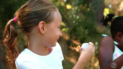 girls blowing bubbles with wand in park