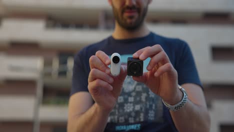 male holding dji action 2 and insta360 go 3 in hands showing size comparison