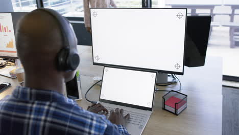 african american businessman using computer and tablet with blank screen, slow motion, copy space