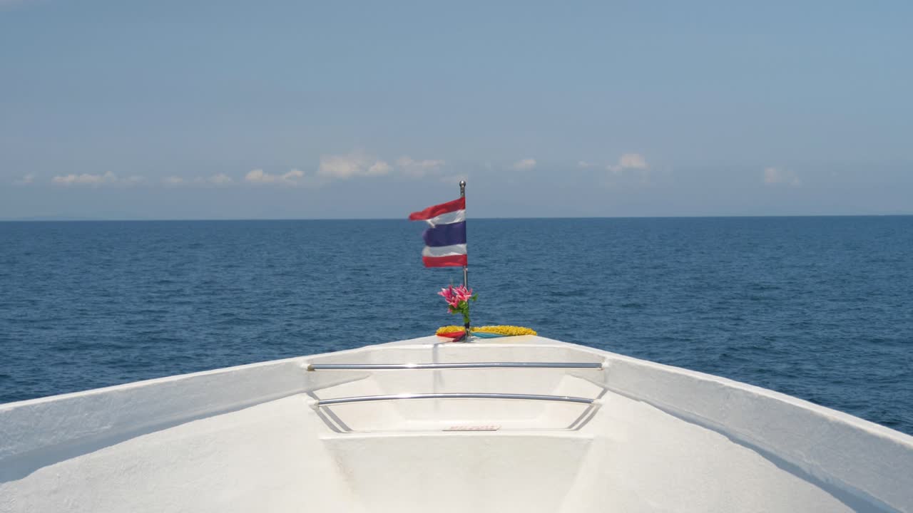 Front view of a ferry boat cutting through the clear Andaman Sea waters with a Thai flag flying