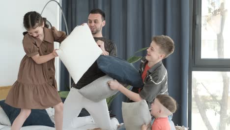 young smiling family fighting with pillows on bed in bedroom young smiling family fighting with pillows on bed in bedroom happy family having fun and playing