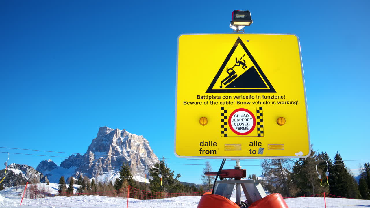 Yellow warning sign about the presence of a potentially dangerous winch cable stretched across the slope on a ski resort