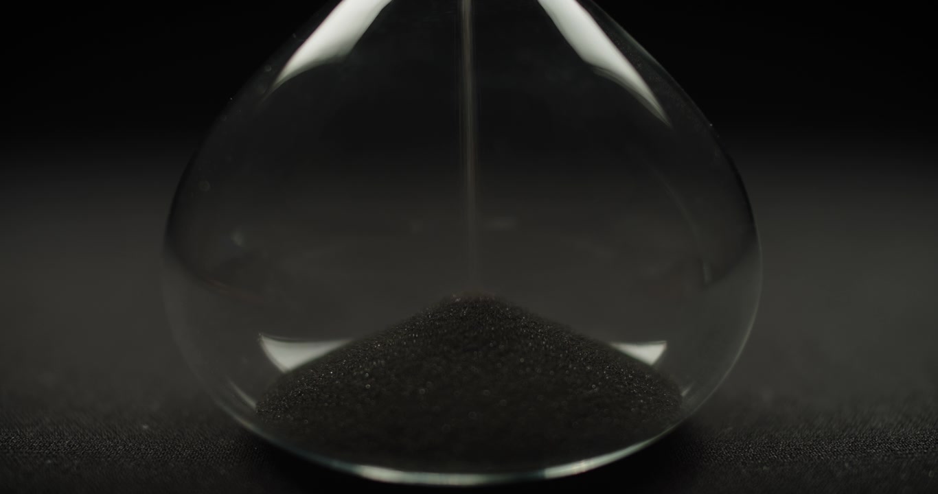 Sabbia nera che scorre all'interno di una clessidra.
