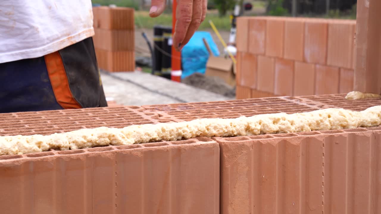 Worker applying adhesive foam to ceramic bricks during construction process