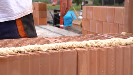 worker applying adhesive foam to ceramic bricks during construction process