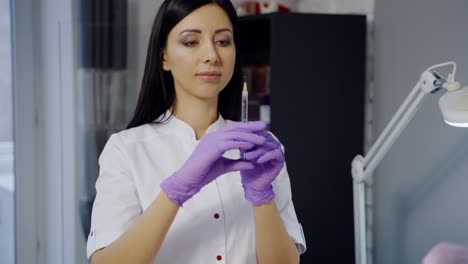 cute cosmetologist with long hair checks a syringe before the botox procedure in the office on the background of a cupboard in a beauty salon.