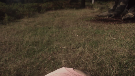 A-close-up-video-of-young-woman-stretching-her-back-to-touch-her-toe-while-sitting-the-grass-on-a-sunny-day