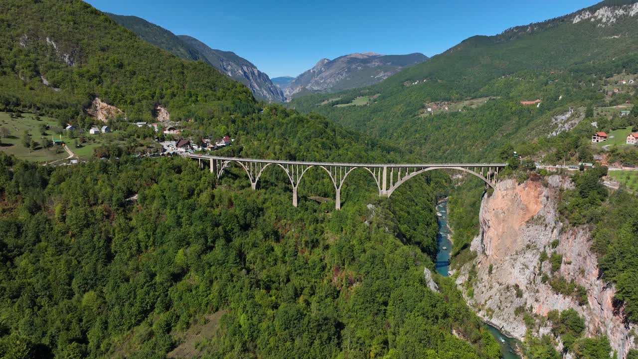 Aerial establishing approach of Tara Bridge spanning the Tara River Gorge in Montenegro, surrounded by lush greenery