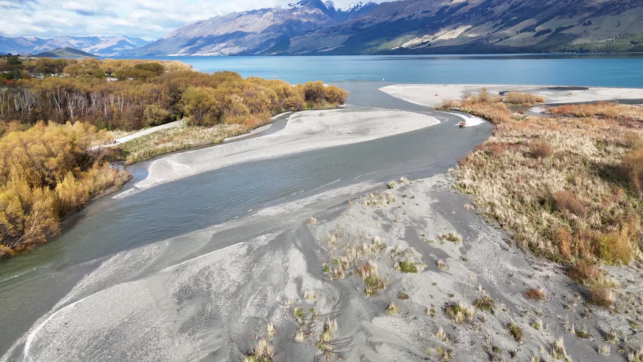 Aerial footage captures the serene riverbend in Glenorchy, New Zealand, with vibrant autumn foliage and majestic mountains under clear skies