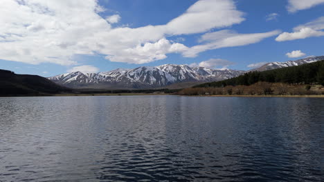 aerial push in over calm waters of laguna la zeta near esquel, argentina, snowcapped mountain ridges and peaks on horizon