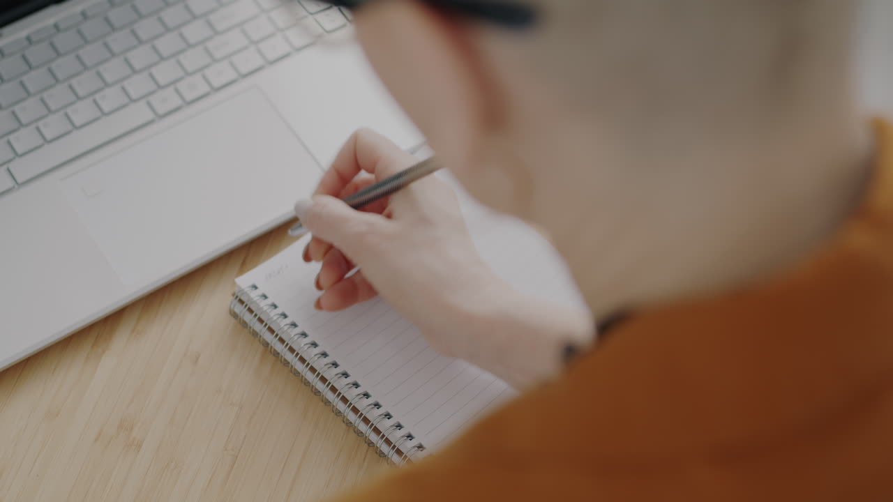 Person Writing in Notebook with Laptop