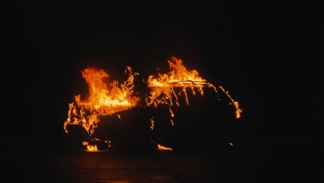car engulfed in flames at night with black background burns with medium flames