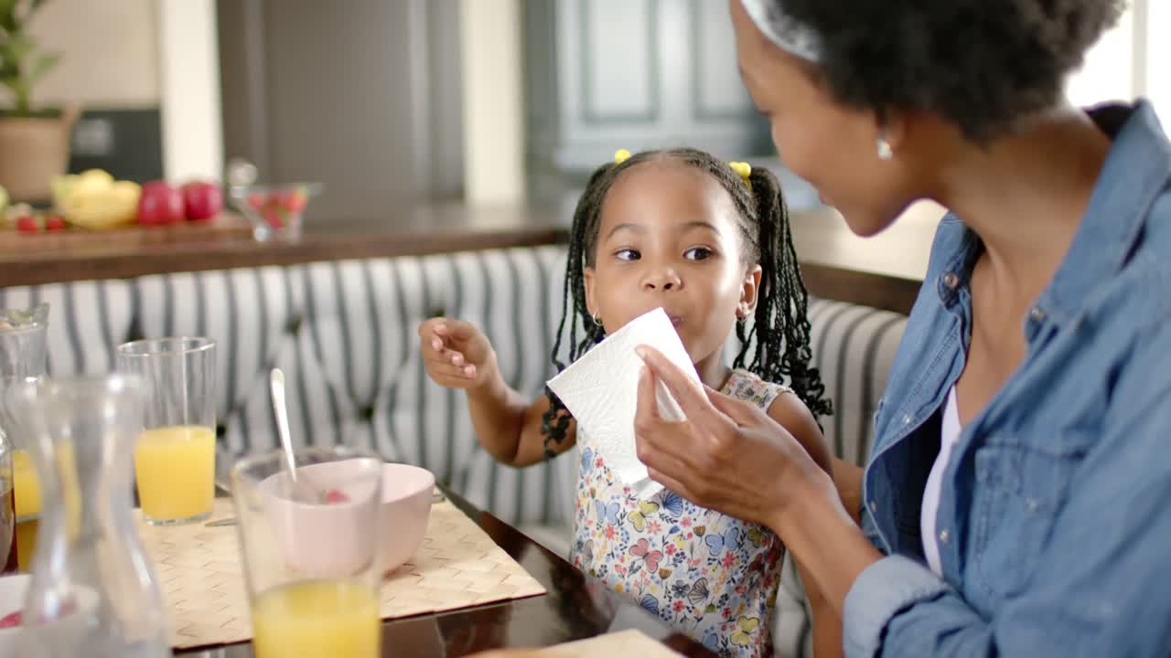 madre y hija afroamericanas felices limpiándose la cara y desayunando, en cámara lenta