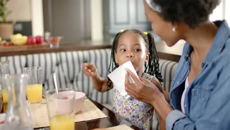 Happy-african-american-mother-and-daughter-wiping-face-and-having-breakfast,-in-slow-motion