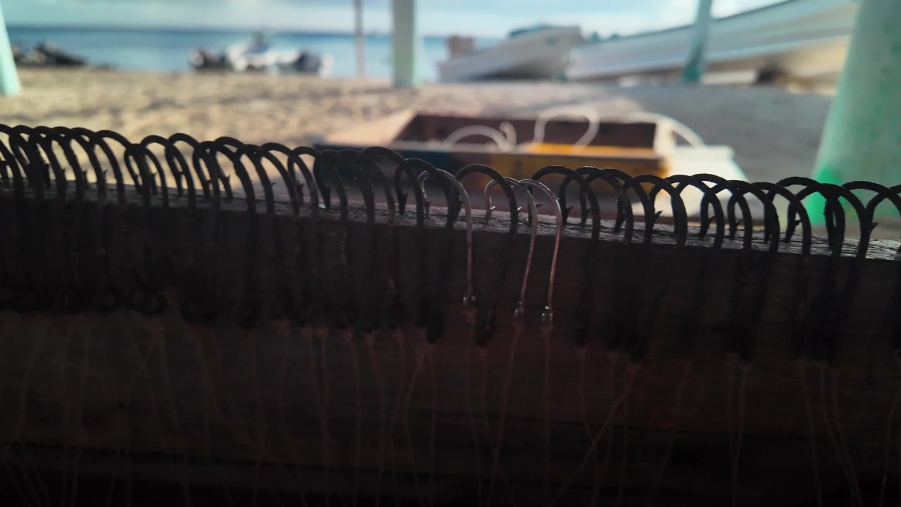 Dettagli macro di ami da pesca organizzati, arrugginiti e nuovi, con spiaggia e barche sfocate sullo sfondo