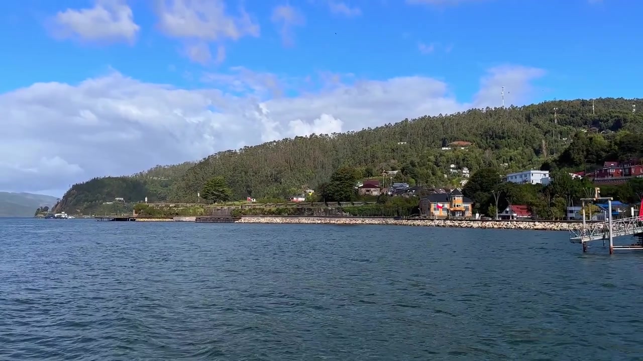 Valdivia, Şili'deki Corral iskelesinin güneşli bir günde, arka planda yemyeşil dağlarla panoramik görünümü