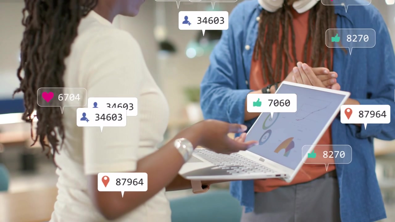 Frau tippt im Büro am Laptop, aufleuchtende Social-Media-Symbole und Diagramme steigern das Engagement, während ein Mann lächelt