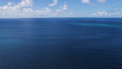 blue pacific ocean waters of hawaii below cloudy sky, drone view