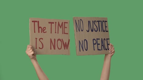 no justice no peace and the time is now. protest text message on cardboard. stop racism. police violence. hands holding a two posters a green screen, chroma key. close up. slow motion