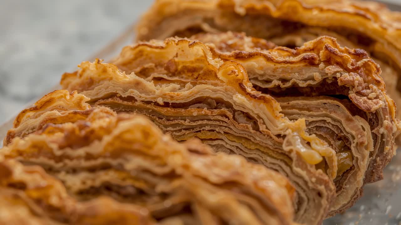 Telecamera che regola la messa a fuoco rivelando strati di pasta sfoglia tagliata su un piano di lavoro chiaro con un piatto trasparente.