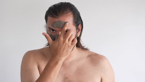 man applies clay facial mask