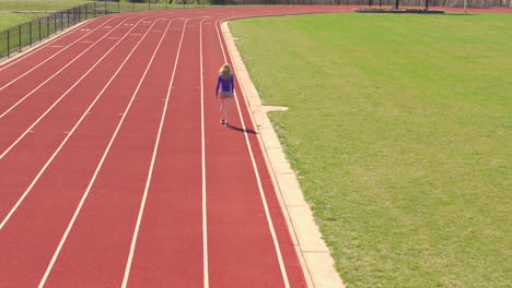 girl on track on a bright and sunny day walks away from camera in slow motion