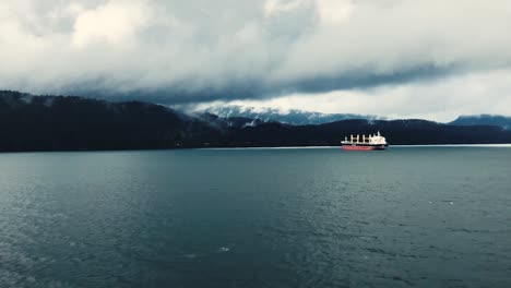 empty bulk carrier equipped with yellow deck cranes in front of the accomodation at the anchorage before the high mountains on a low hanging cloudy day