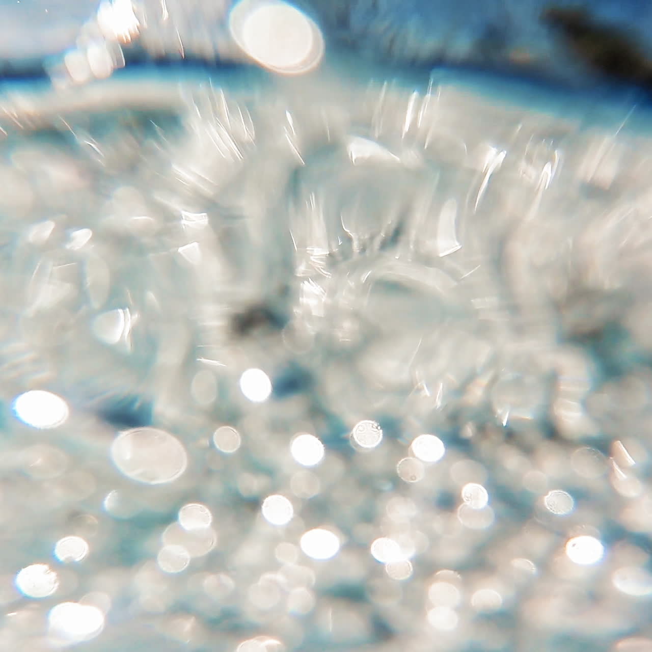 Clear water falling into the pool. Waterfall over the pool making air bubbles on water surface outdoors in sunny day. Close-up.