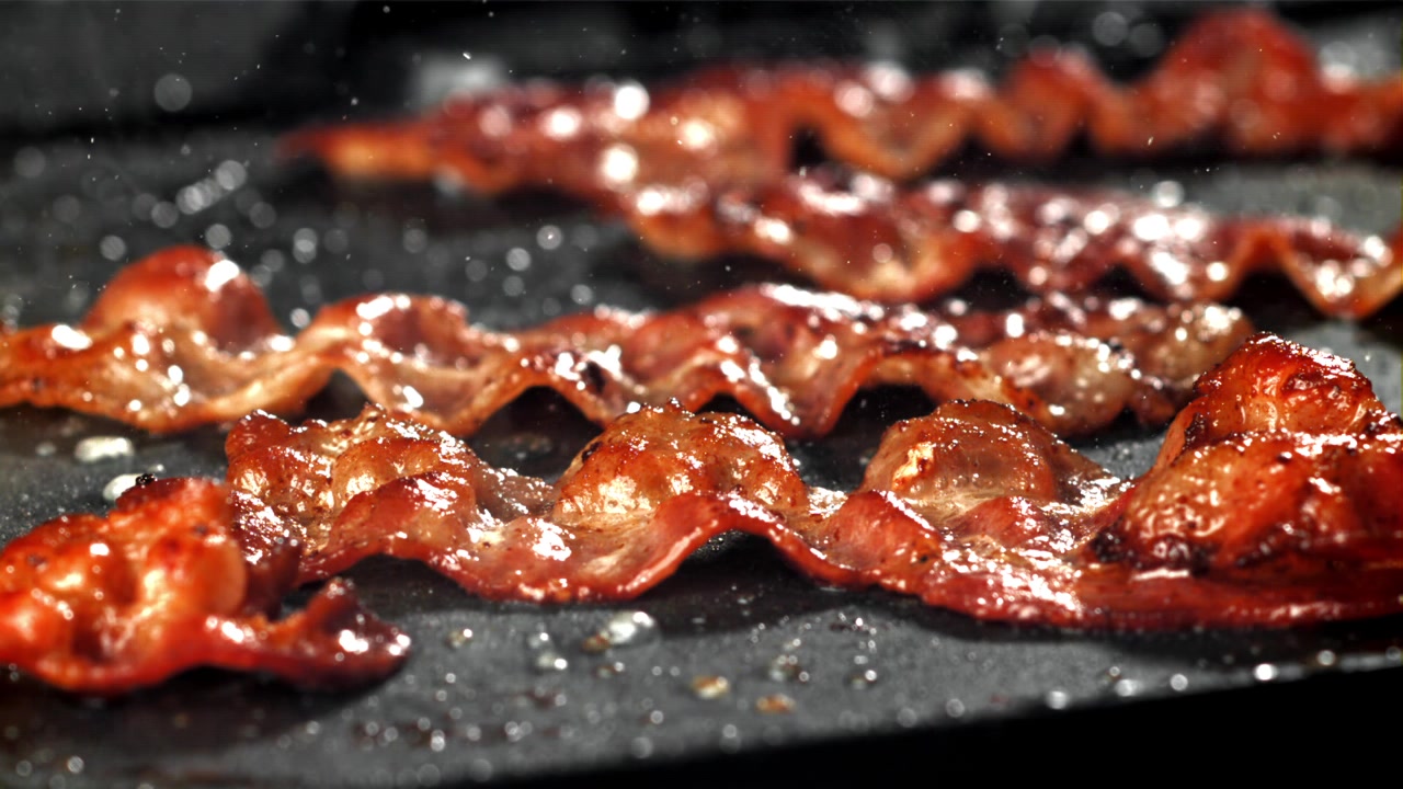 Strisce di pancetta sfrigolanti che friggono in una padella calda