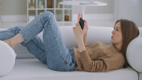 woman on a video call using a mobile phone. mature woman with talking on smartphone while sitting at living room with modern interior. concept of technology and relaxation.