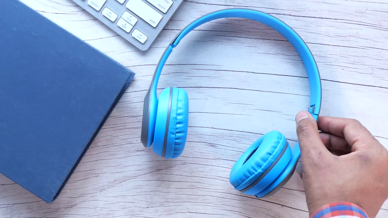 auriculares azules en un escritorio de madera con teclado y libro