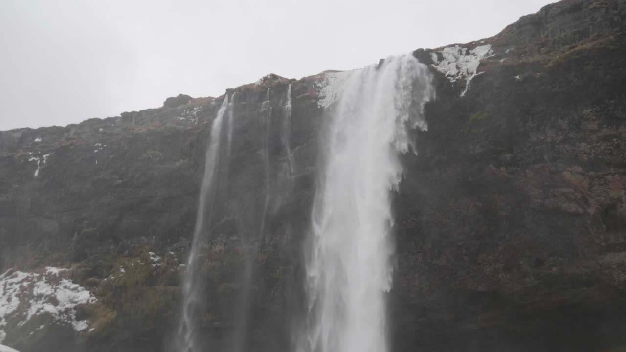 estática, cámara lenta, tiro inclinado, de agua que cae sobre suelo nevado, en la cascada de seljalandfoss, en un día nublado de otoño, en la costa sur de islandia