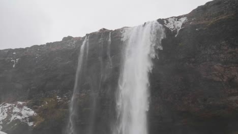 Estático,-Cámara-Lenta,-Tiro-Inclinado,-De-Agua-Que-Cae-Sobre-Suelo-Nevado,-En-La-Cascada-De-Seljalandfoss,-En-Un-Día-Nublado-De-Otoño,-En-La-Costa-Sur-De-Islandia