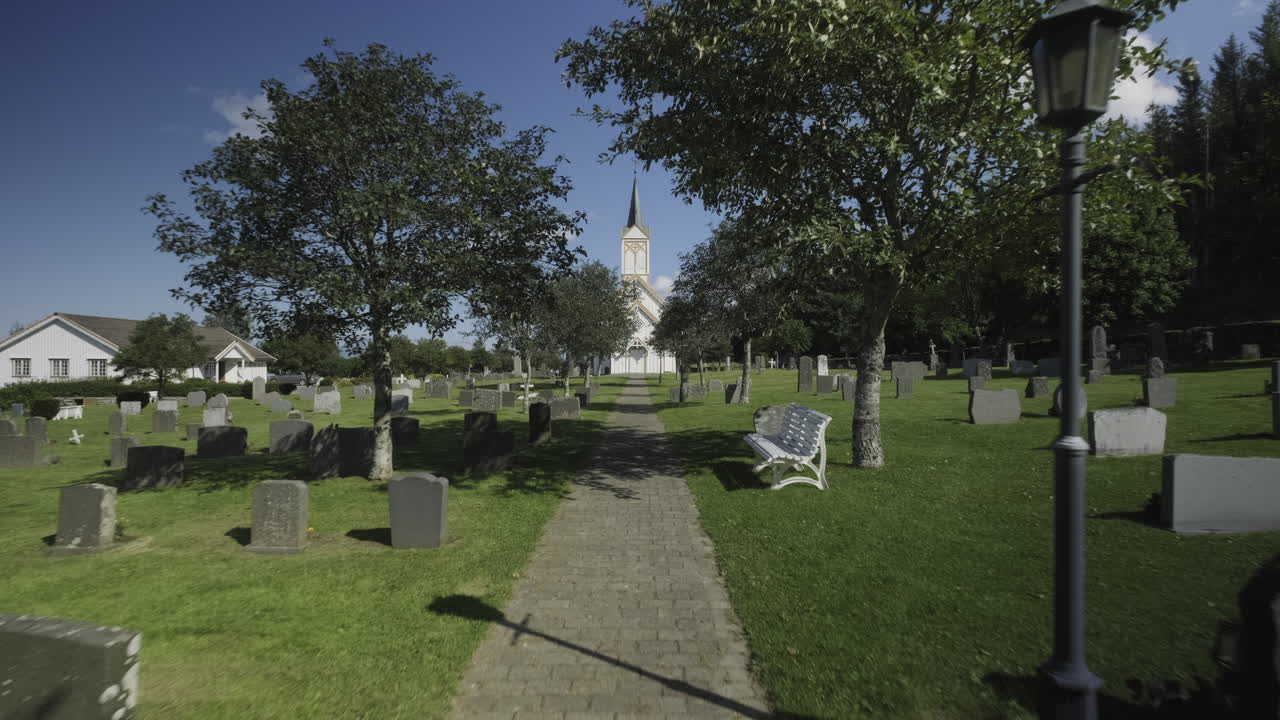 Inquadratura in avvicinamento di un cimitero con una piccola e accogliente chiesa norvegese in lontananza