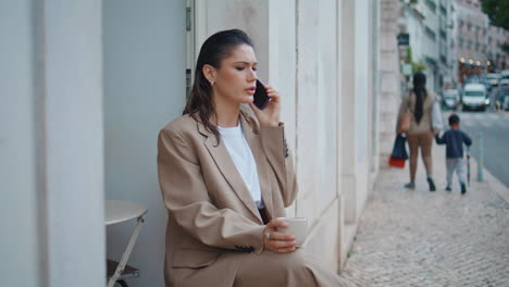 trendy girl calling mobile phone at outdoors cafe holding coffee cup close up.