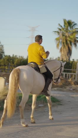 man riding a white horse outdoors, smiling and giving a thumbs up
